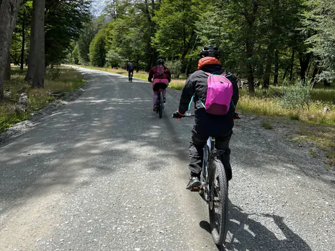 Tres riders con casco pedalean en e-Bike por un camino de ripio entre árboles, camino al río Mayer