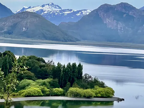 El lago Cisnes desde lo alto, con una península de árboles y cerros nevados al fondo