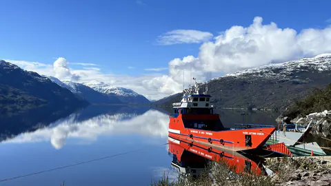 La barcaza roja en el fiordo Mitchell, entre cerros nevados reflejados en el agua