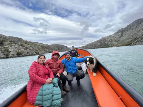Una familia y su perro sentados en la proa de una lancha naranja, navegando el lago entre cerros