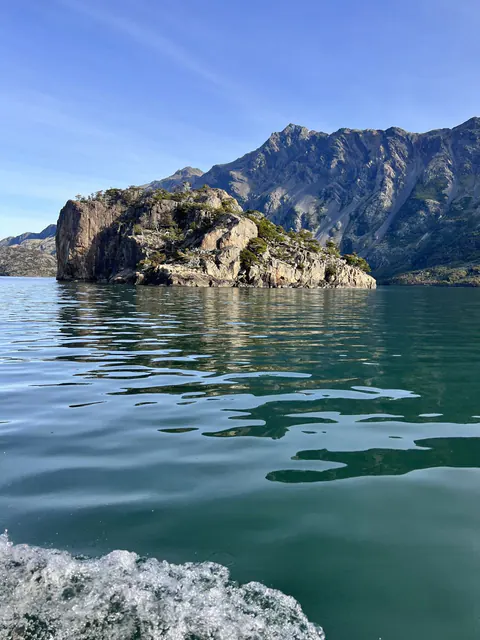 Una isla de roca en medio del agua verde del lago, con cerros al fondo