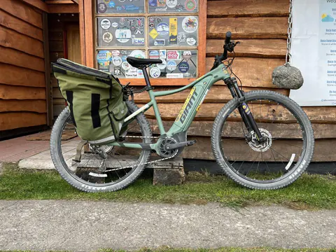 Una e-Bike SURí con alforjas apoyada en una casa de madera