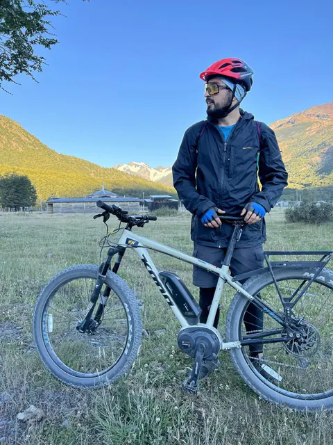Un rider de pie junto a su e-Bike en un prado, con cerros detrás