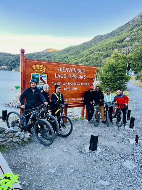 Un grupo de ciclistas con sus e-Bikes junto al cartel de bienvenida al lago O'Higgins, fin de la Carretera Austral
