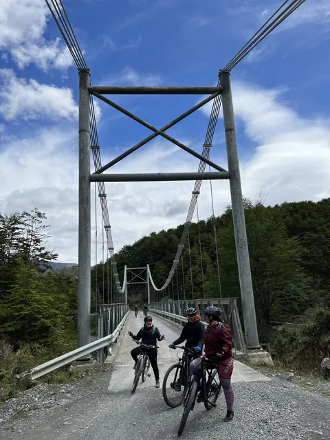 Tres riders con casco y sus e-Bikes en un puente colgante, entre el bosque