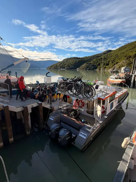 Viajeros con casco esperan en el muelle de Puerto Bahamondes mientras las bicicletas se cargan en el techo de una lancha de Ruedas de la Patagonia