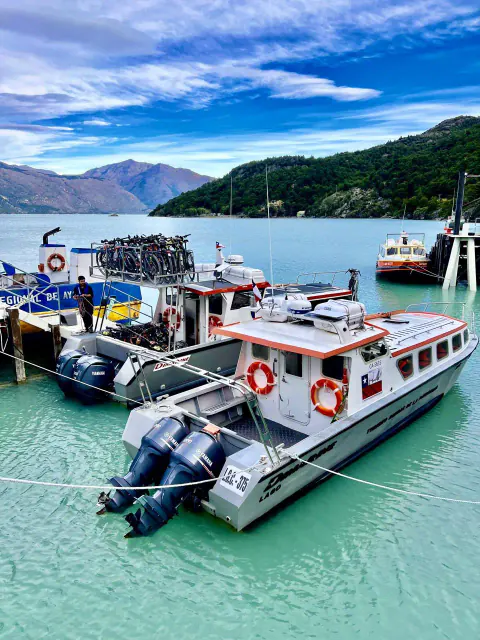 Dos lanchas blancas de Ruedas de la Patagonia amarradas en el muelle de Puerto Bahamondes, con bicicletas cargadas en el techo, sobre el agua turquesa del lago O'Higgins
