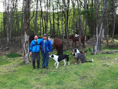 Javi y Ricardo Levicán de pie en un claro del bosque, con caballos y dos perros, camino al Lago del Desierto