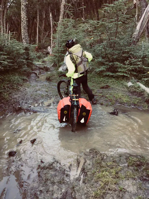 Un ciclista empuja su bici con alforjas por un tramo inundado del sendero, en el bosque