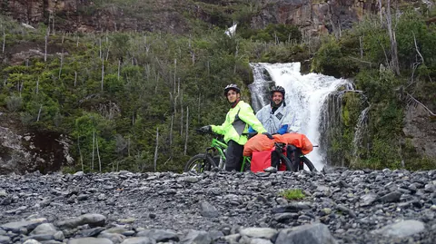 Javi y Nacho con sus bicicletas cargadas frente a una cascada