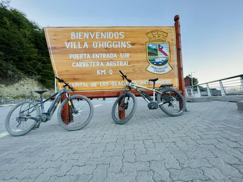 Dos e-Bikes frente al cartel de bienvenida a Villa O'Higgins, km 0 de la entrada sur de la Carretera Austral