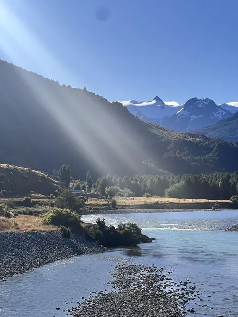 Un río de piedras bajo un cerro, con rayos de sol entre las nubes