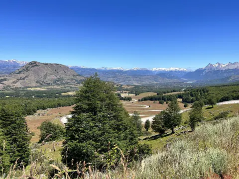 Un valle ancho con un río que serpentea entre bosques y pampas, con cerros al fondo