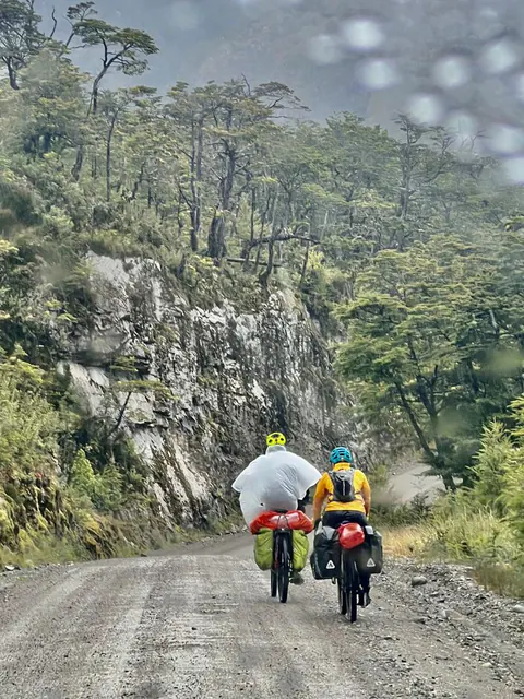 Dos riders con casco y alforjas pedalean por el ripio, entre paredes de roca y bosque